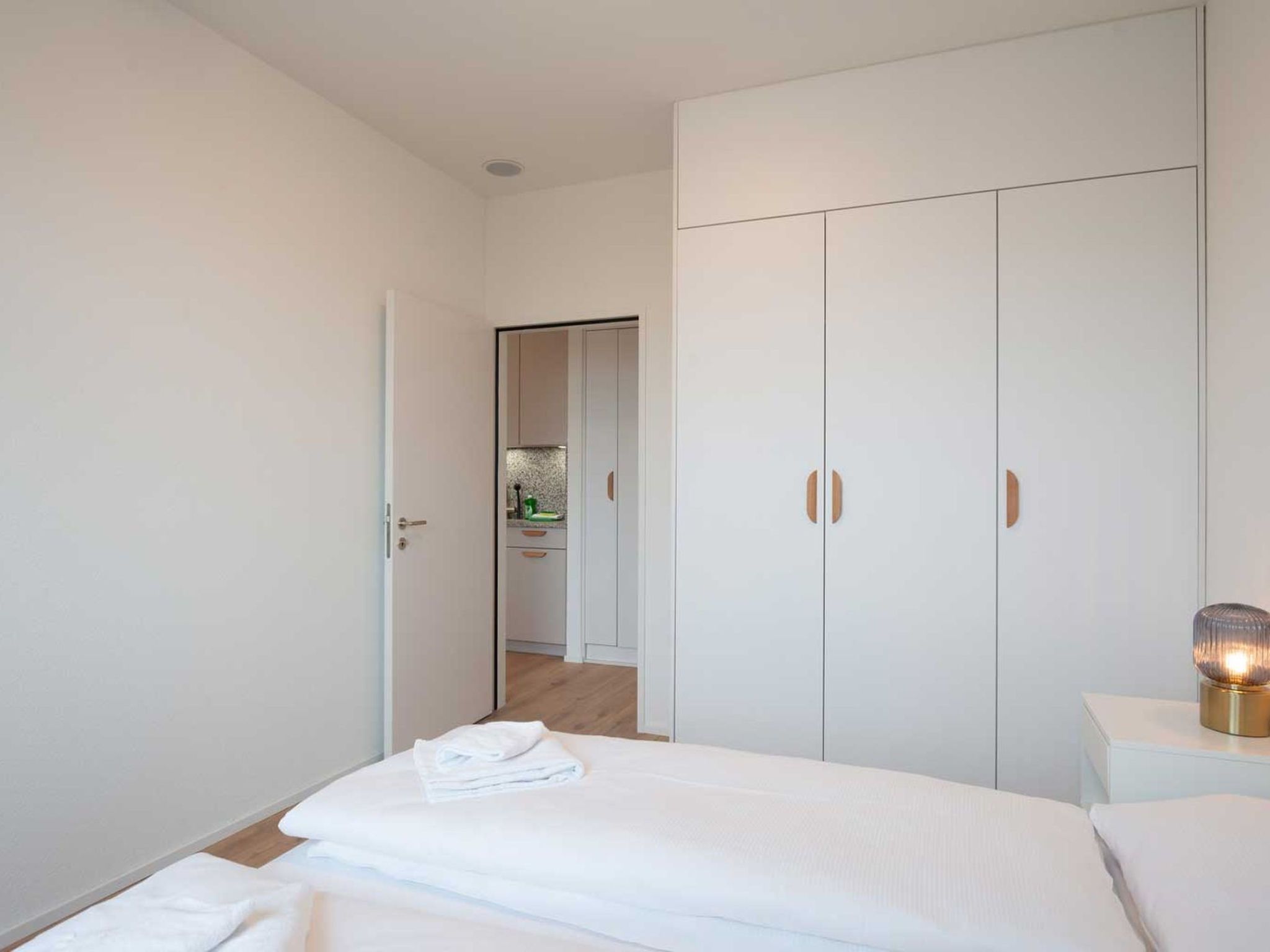 A bedroom with a bed, a wardrobe, and a bedside table with a lamp.