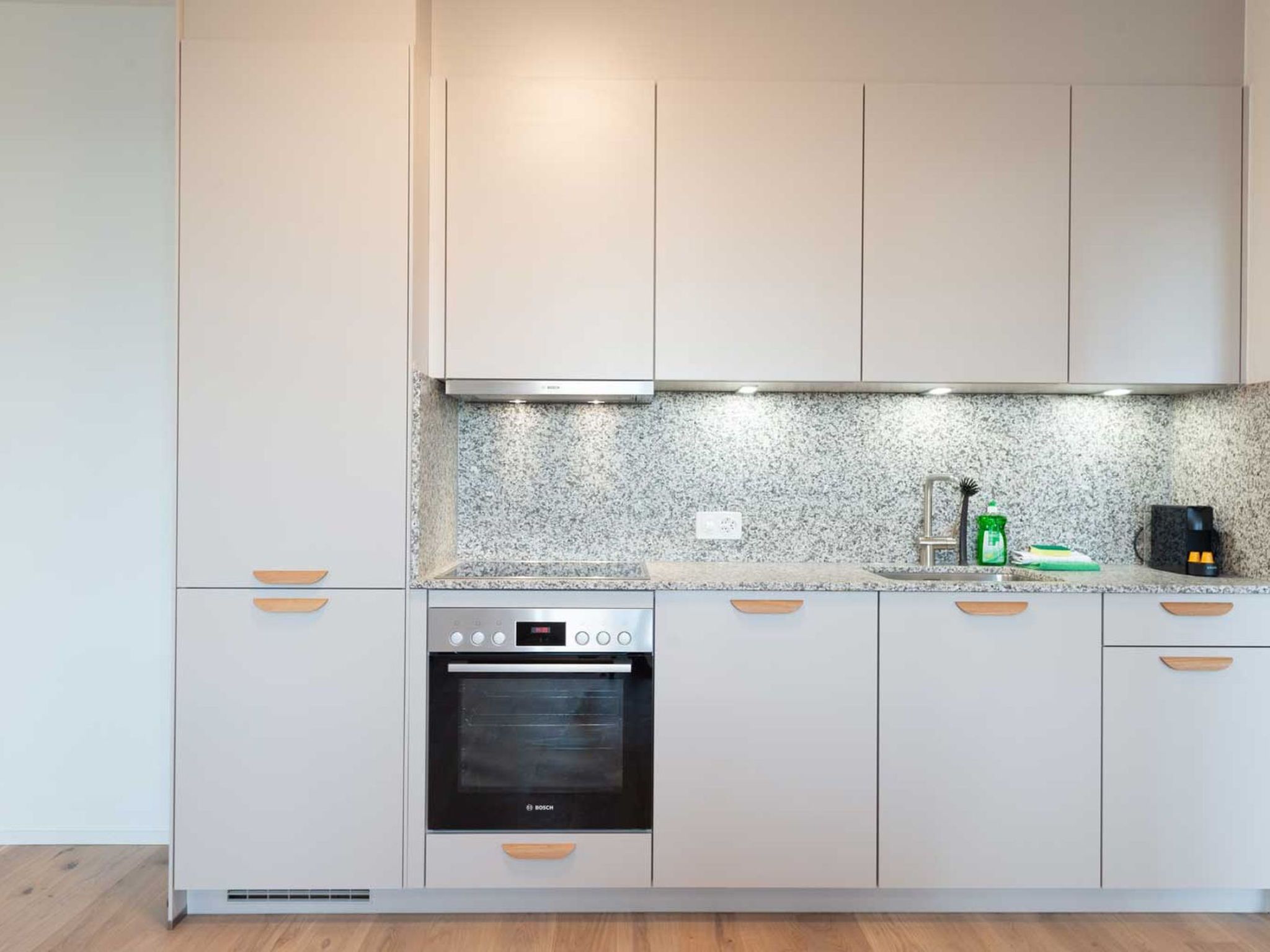 A kitchen with white cabinets, a Bosch oven, a granite countertop, and a coffee maker.