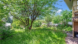 Ein Garten mit Bäumen, einer Holzterrasse und einem Gebäude mit schrägem Dach.