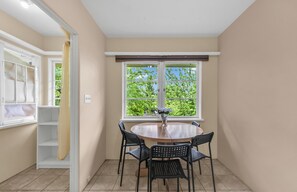 A room with a round table, four chairs, a window with a view of greenery, and a white door with a curtain.