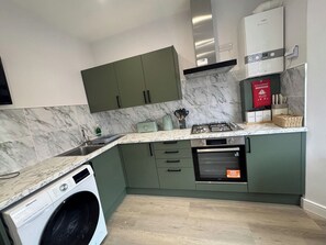 Een kleine keuken met een wasmachine, gasfornuis en een inbouwoven.