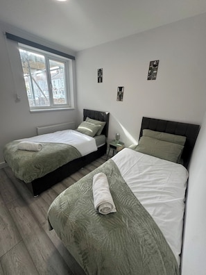 A bedroom with two beds, a window, and a radiator. - Home In Bedford Fast Wifi | Parking |Contractors (Bedford)