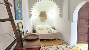 A narrow room with a bed, a decorative wall, and a wooden ladder.