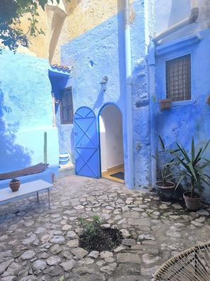 A courtyard with a stone floor, a blue door, and potted plants. - Riad Louisa Chaouen (Chefchaouen)