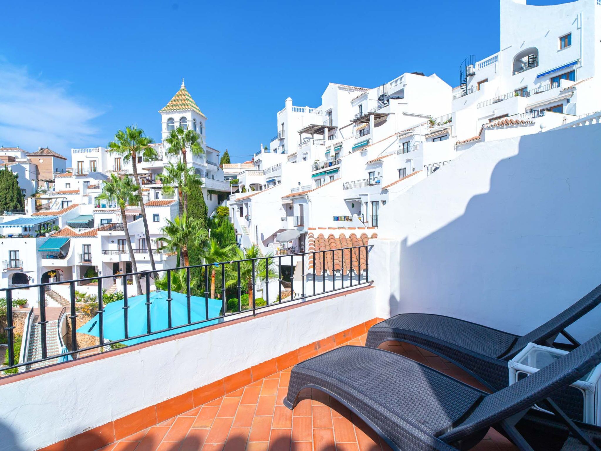 Un balcon donnant sur un ensemble d’immeubles blancs, une piscine et un palmier.