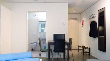 Une chambre moderne comprenant un lit, un bureau avec une chaise, une petite salle de bain et un porte-manteau.