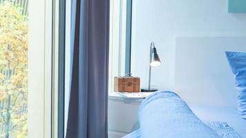 A bed with a headboard, a bedside lamp, a small wooden box, and a window with curtains.