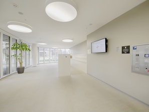 A modern, well-lit hallway with a reception desk, a mounted screen, and a control panel. - LU KKL I - Allmend HITrental Apartment by Interhome (Lucerne)