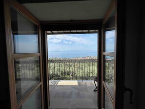 An open balcony with a view of a coastal landscape, a tiled floor, and a metal railing.