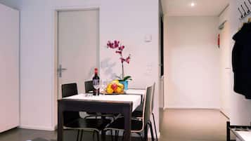 A small, modern room with a dining table set for two, a potted orchid, and a fruit bowl.