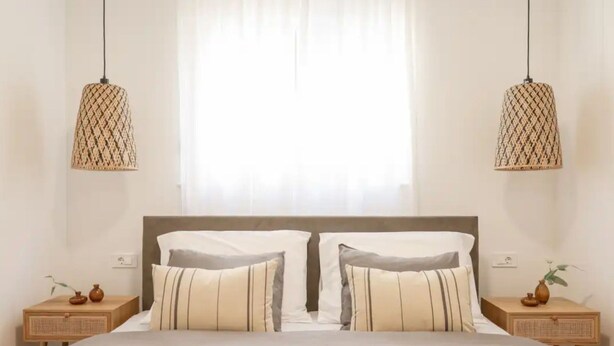 Une chambre à coucher avec un grand lit, deux tables de chevet, une fenêtre avec des rideaux et deux lampes suspendues.