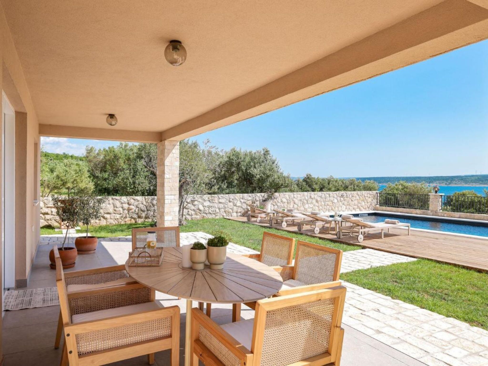 A covered outdoor area with a pool, a table with chairs, and a view of the sea.