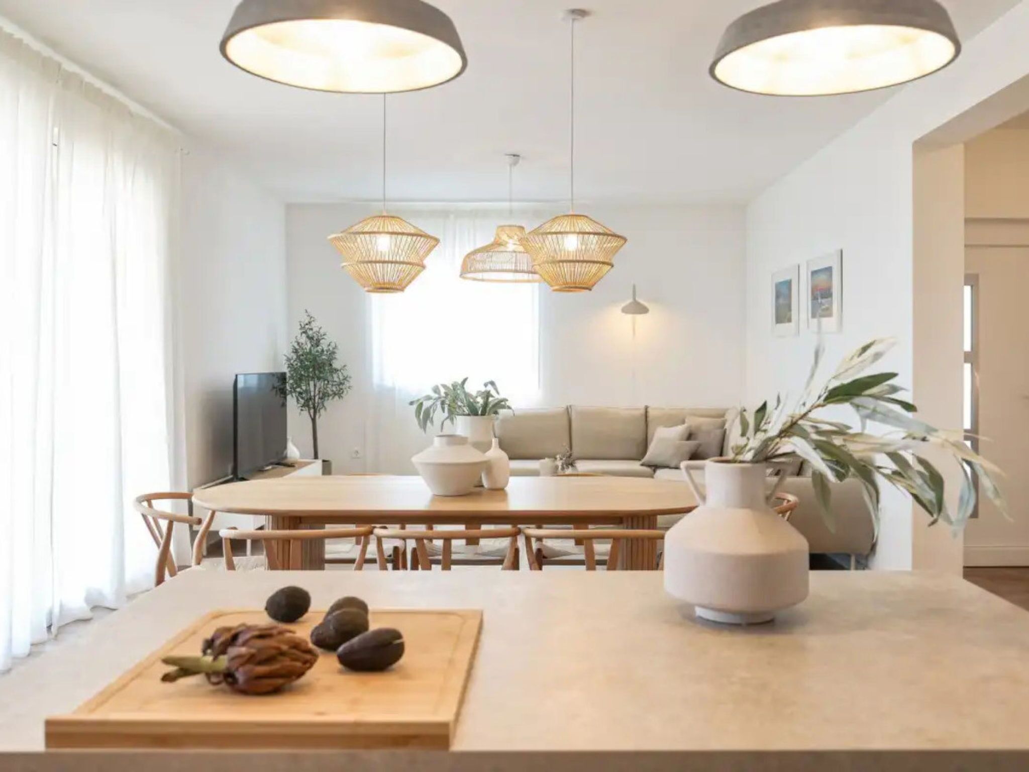 A modern dining area with a central table, chairs, and hanging rattan light fixtures.