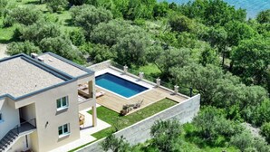Une maison moderne à deux étages, dotée d’une piscine, entourée d’une végétation luxuriante et offrant une vue sur la mer.