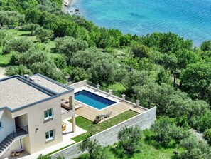 Ein modernes, zweistöckiges Haus mit Swimmingpool, umgeben von üppiger Vegetation und Blick aufs Meer.