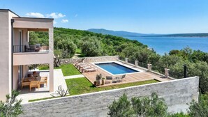 Un bâtiment moderne à deux étages, doté d’une piscine, de mobilier d’extérieur et offrant une vue sur la mer.