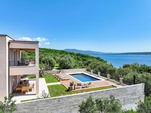 Ein modernes, zweistöckiges Gebäude mit Pool, Gartenmöbeln und Meerblick.