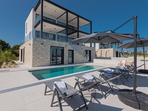 Ein modernes, zweistöckiges Haus mit Swimmingpool, Sitzgelegenheiten im Freien und einer Stein-Fassade.