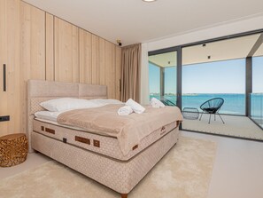 Een moderne slaapkamer met een groot bed, houten lambrisering en een balkon met uitzicht op zee.