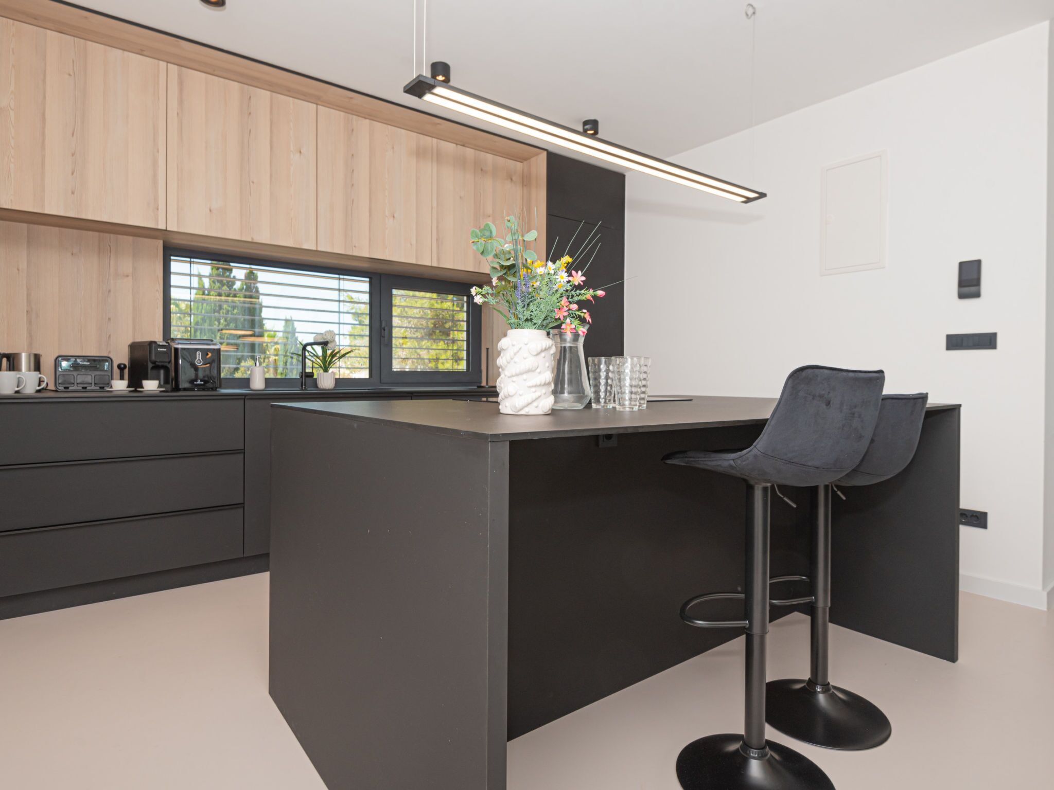 A modern kitchen with a central island, bar stools, and a window with blinds.