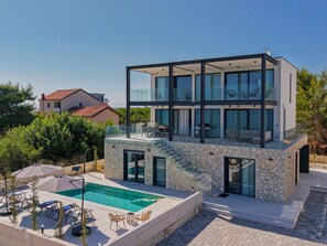 Een modern herenhuis met twee verdiepingen, een glazen gevel, een stenen buitenkant en een zwembad met buitenzitplaatsen.