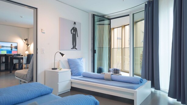 A modern hotel room with a bed, bedside table, lamp, and a large window with curtains. - Apartment  by Interhome (Lucerne)