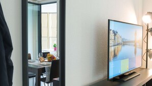 A modern room with a television displaying a cityscape, a dining area with a table and chairs, and a large mirror reflecting the room. - Apartment  by Interhome (Lucerne)