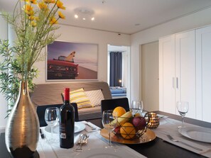 A hotel room with a dining table set for two, a bottle of wine, a fruit bowl, and a bed with a view of a beach. - Apartment  by Interhome (Lucerne)