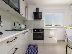 Une cuisine moderne avec des meubles blancs, un four encastré et une fenêtre offrant une belle vue.