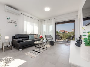 Un salon moderne avec un canapé, une petite table et un fauteuil. Il y a un balcon qui offre une vue sur les immeubles.