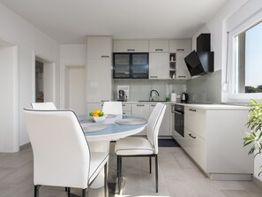 Une cuisine moderne avec des meubles blancs, une table à manger avec des chaises et une fenêtre laissant entrer la lumière naturelle.