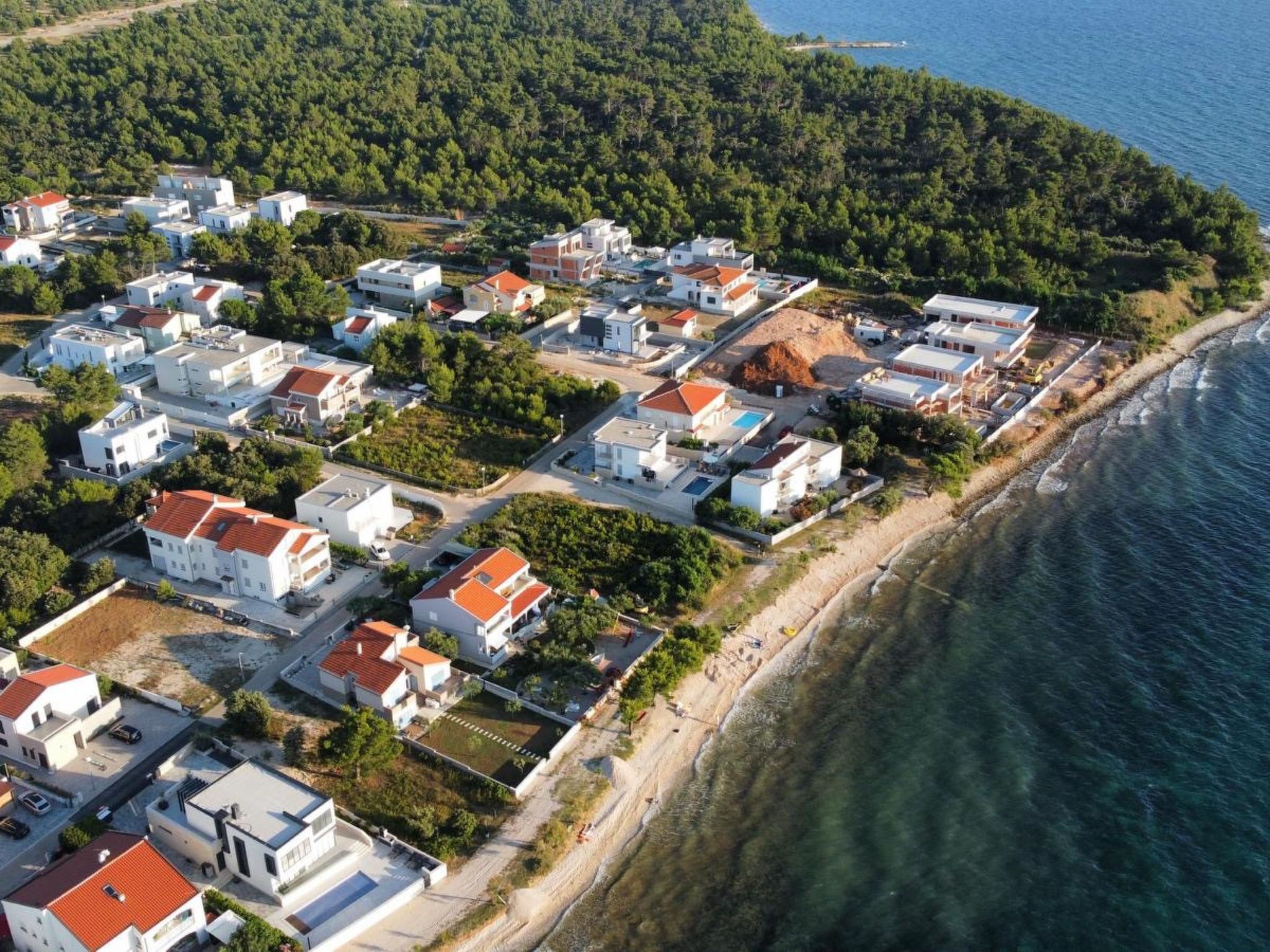 An aerial view of a coastal residential area with houses, a beach, and a forested hill.