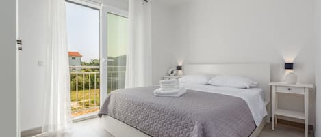 Un dormitorio moderno con una cama grande, una mesita de noche, una lámpara de noche y vistas al exterior.
