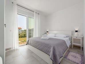 A modern bedroom with a large bed, a nightstand, a bedside lamp, and a view of the outdoors. - Apartment  by Interhome (Nin)
