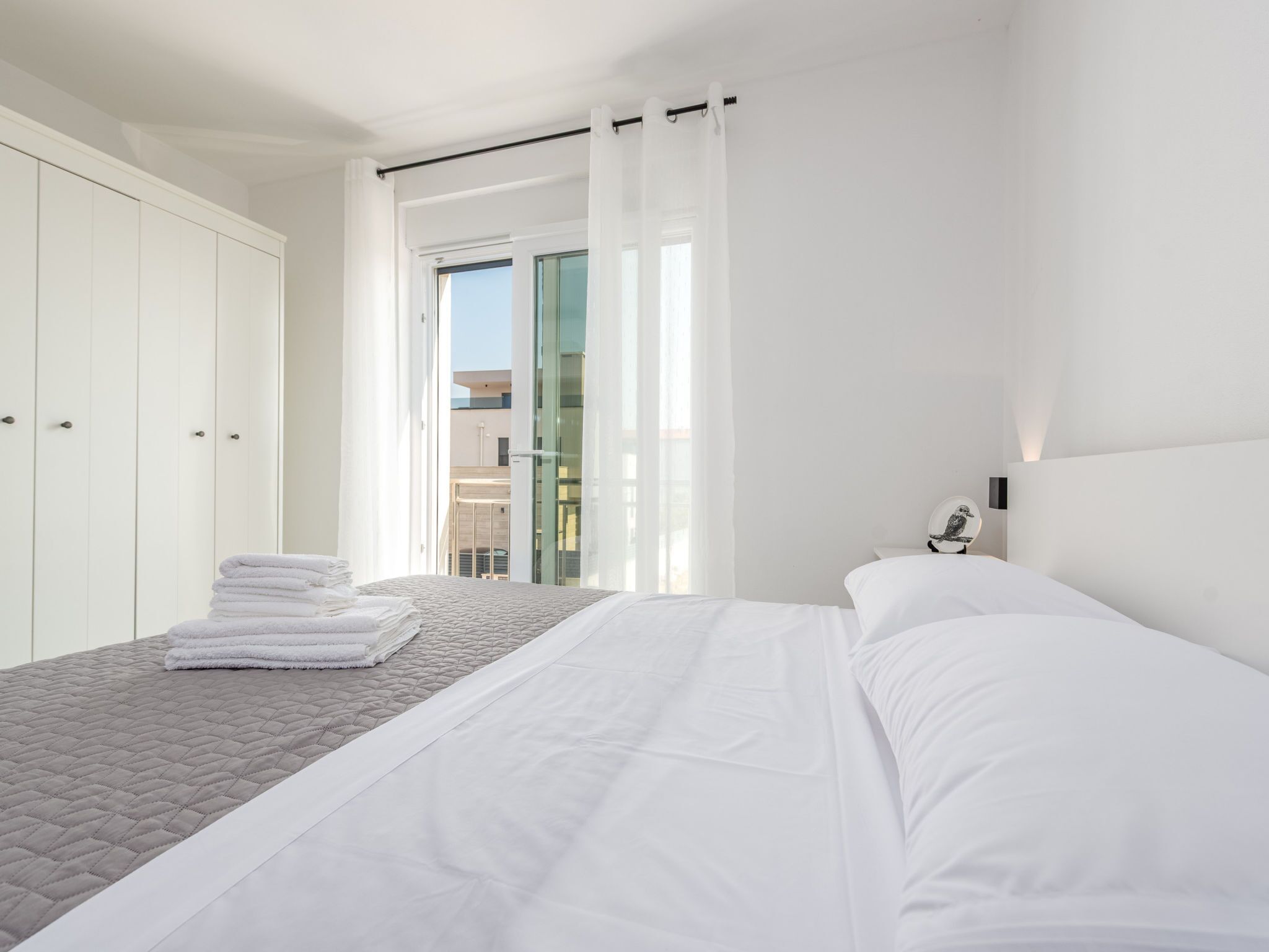 Une chambre d’hôtel avec un lit, une pile de serviettes, une table de chevet avec une lampe et une vue sur un immeuble par la fenêtre.