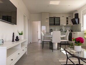 A modern kitchen with white cabinets, a dining area with a glass table and chairs, and a TV mounted on the wall. - Apartment Laurel near the sea by Interhome (Nin)