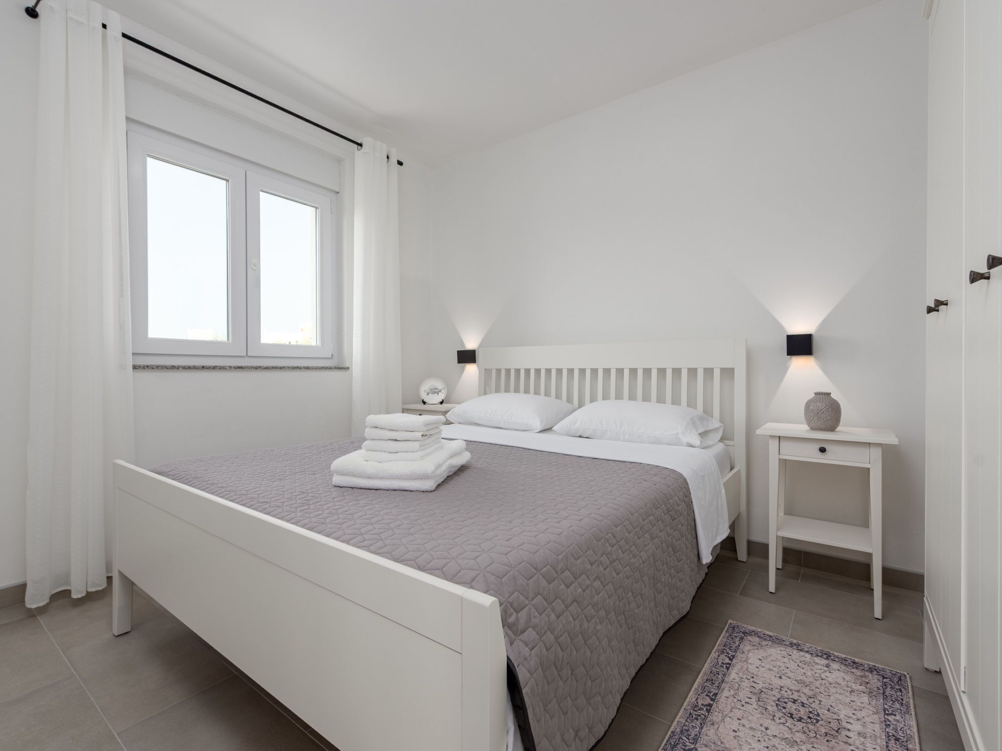 A bedroom with a bed, a nightstand, a lamp, and a window.