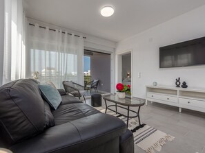 Un salon moderne avec un canapé en cuir noir, une table basse en verre et un meuble TV blanc.