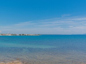 A coastal view with clear blue water, a sandy beach, and buildings in the distance. - Seafront Villa Serena with pool and seaview by Interhome (Privlaka)