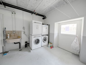 A laundry room with two washing machines, a sink, and a window. - Apartment  by Interhome (Zurich)