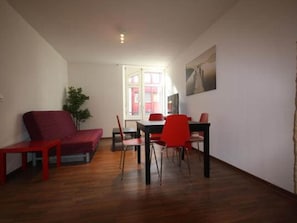 A room with a red sofa, a dining table with chairs, a potted plant, and a window. - ZH Blueberry l - Oerlikon HITrental Apartment by Interhome (Zurich)