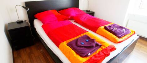 A double bed with a black headboard, white bedding, and two pillows with colorful blankets.