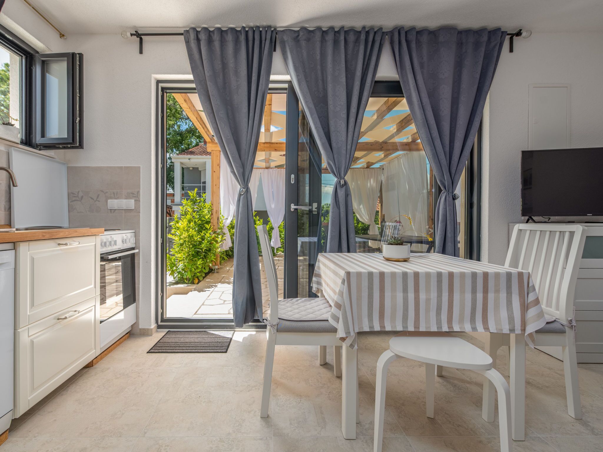 A modern kitchen with a dining area, a TV, and a view of the outdoors.