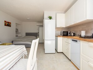 Ein gemütliches Schlafzimmer mit Bett, Nachttisch und Stuhl. Angrenzend befindet sich eine Küchenzeile mit Mikrowelle, Wasserkocher und Kühlschrank.