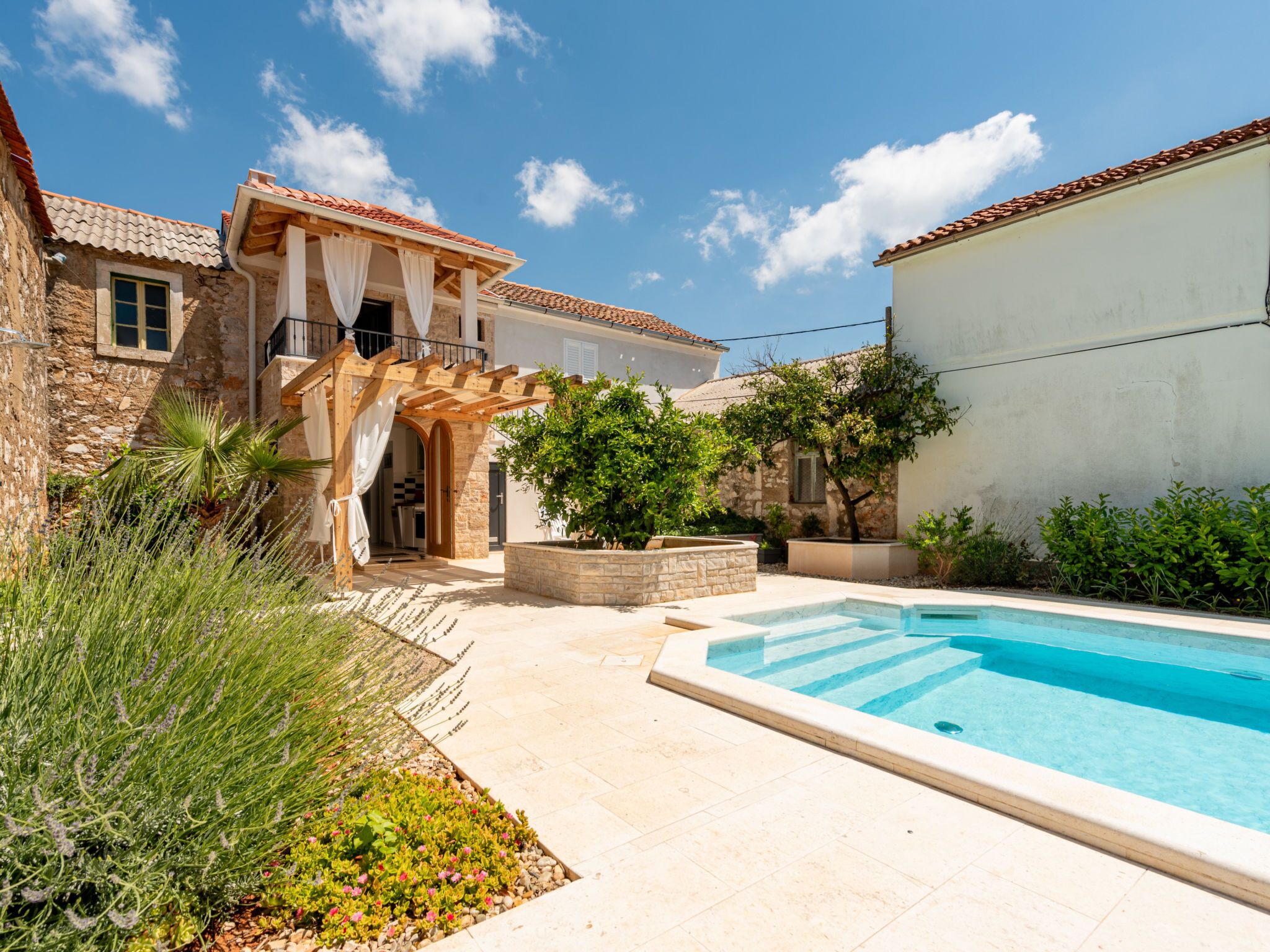 A courtyard with a swimming pool, stone buildings, and a pergola.