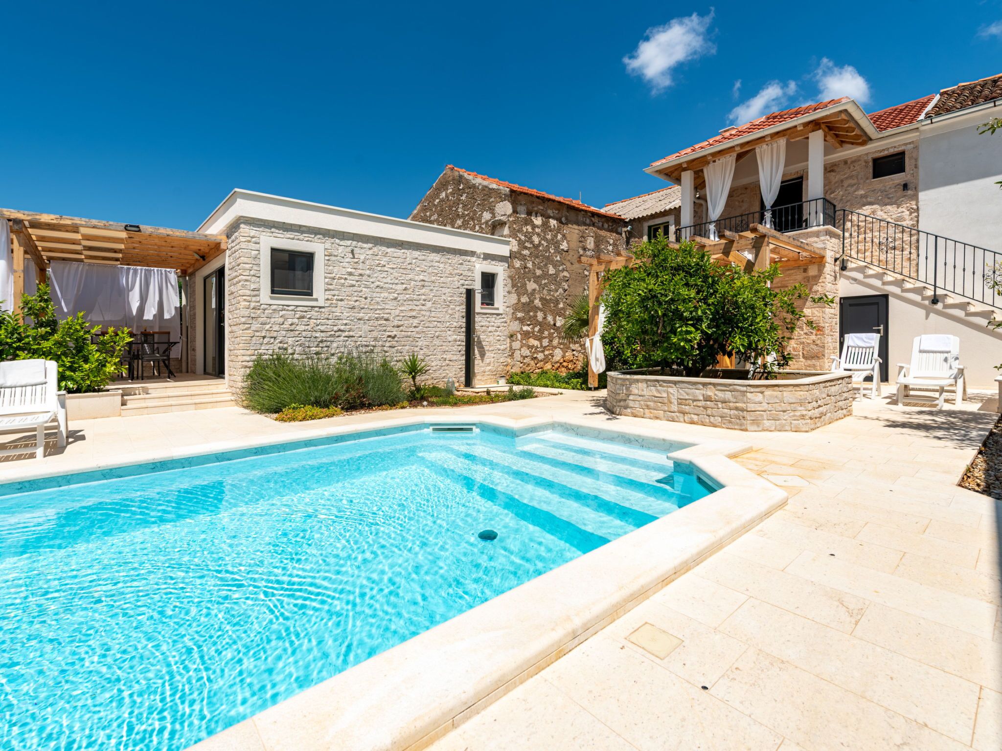 A swimming pool with a stone wall and a wooden pergola.