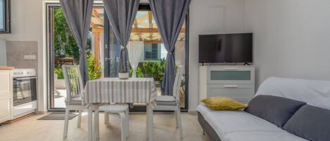 Quarto moderno com uma cama, televisão e área de refeições com mesa e cadeiras.
