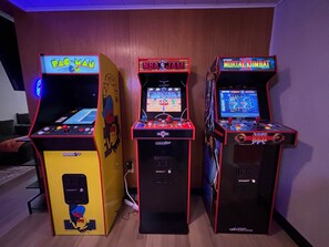 Tres máquinas de arcade en una habitación con paredes de madera y un televisor de pantalla plana al fondo.