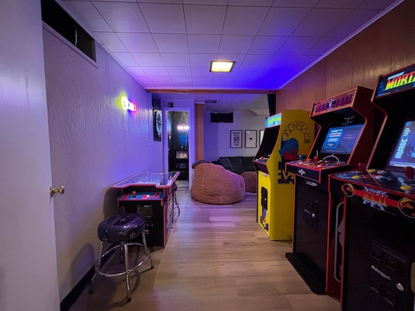Un pasillo con máquinas de videojuegos, una mesa de ping pong y un sillón de mimbre.