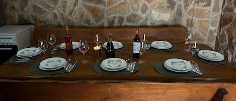 A stone wall with a framed certificate, a wooden table set for dining with plates, glasses, and cutlery, and a bench in the background.